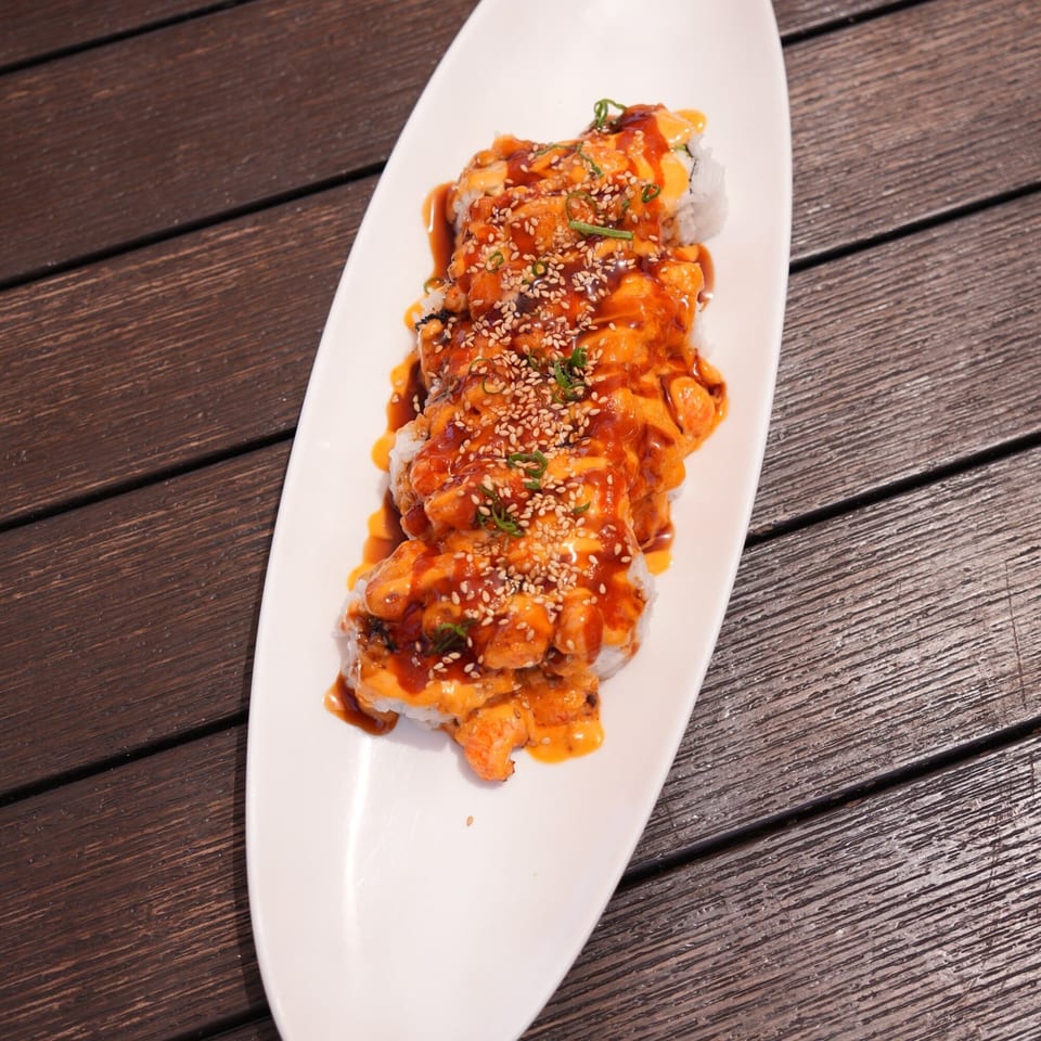 Higo Sushi's sushi rolls topped with spicy orange sauce, sesame seeds, and green onions on a white plate.