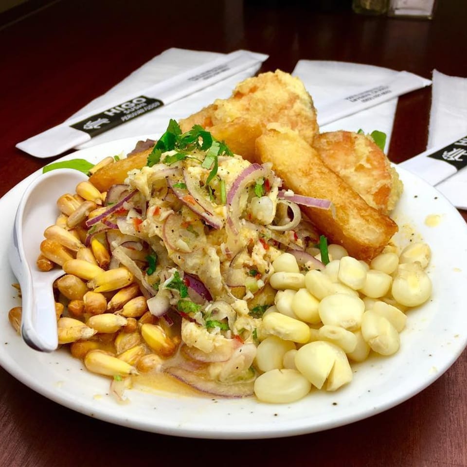 Higo Sushi and Peruvian ceviche with red onions, corn, and fried plantains on a white plate.