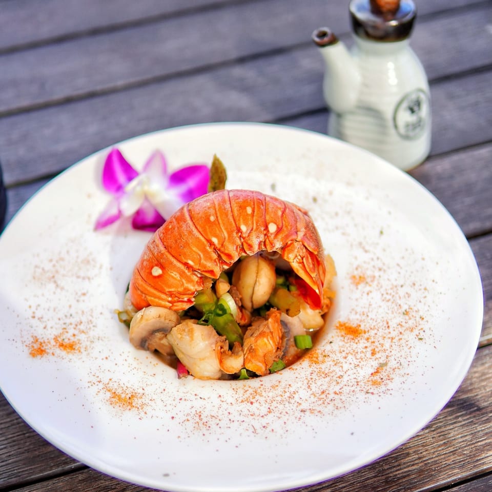 A Higo Sushi and Peruvian dish with a lobster tail, mushrooms, and green onions, garnished with a purple orchid.